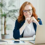 Pleased cheerful female economist develops financial startup project poses in office interior